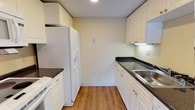 This 2-bedroom, 2-bathroom residence is thoughtfully laid out across a single floor, offering a comfortable and functional living environment. The kitchen is a standout feature, showcasing white shaker-style cabinetry that extends to the ceiling for generous storage capacity. Dark granite-look countertops provide a striking contrast against the white cabinetry and are complemented by a stainless steel sink. White appliances, including a refrigerator with an ice and water dispenser and a dishwasher, are seamlessly integrated into the space. Warm wood-style flooring runs throughout the kitchen, adding a welcoming and cohesive aesthetic. The neutral, light-toned walls create a bright and airy atmosphere, allowing natural light to enhance the overall ambiance. The galley-style kitchen layout maximizes efficiency, making it well-suited for everyday cooking and meal preparation. The two bedrooms offer private retreats, while the two full bathrooms provide convenience for both residents and guests. The single-floor layout ensures easy accessibility and a smooth, connected flow between living spaces, making this a practical and inviting home.