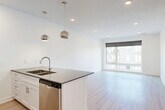 Located at 3001 Leavenworth St in Omaha, Nebraska, this modern one-bedroom, one-bathroom unit offers a clean, contemporary design throughout. The open-concept kitchen and living area serves as the heart of the home, featuring light wood-look flooring that extends seamlessly across the space. The kitchen is outfitted with white shaker cabinetry, dark quartz countertops, a full suite of stainless steel appliances including a refrigerator, range, microwave, and dishwasher, and a peninsula island topped with a double undermount sink and illuminated by sleek chrome globe pendant lights. The living area is bright and airy, bathed in natural light from large floor-to-ceiling windows that frame views of the surrounding Omaha cityscape. The bedroom offers plush carpeting, a ceiling fan, and generous natural light through expansive windows, while two closets — including a walk-in with wire shelving — provide ample storage. The bathroom is well-appointed with white shaker vanity cabinetry, a dark quartz countertop, an undermount sink, a wide mirror, and a full tub-shower combination. Recessed lighting throughout and crisp white walls give the entire unit a bright, polished ambiance.