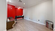 Located at 721 S Cherry Grove Ave in Annapolis, Maryland, this single-floor business center offers a well-appointed and efficiently organized workspace. The room features light wood-look flooring and crisp white crown molding that runs along the perimeter, lending a clean, polished appearance to the interior.

A bold red accent wall serves as the focal point, adding a vibrant, energetic contrast to the otherwise neutral gray-and-white color palette. Built-in granite-topped desks with elegantly curved bases line two walls, providing dedicated workstations equipped with desktop computers and a multifunction printer — ideal for residents or tenants needing printing, scanning, and computing resources.

Recessed lighting throughout the ceiling ensures the space is well-illuminated, while a window and a glass-paneled door invite natural light and offer views of a lush outdoor courtyard area. The door is equipped with a keycard access system and an automatic door opener, ensuring secure and convenient entry and exit. A wall-mounted hand sanitizer dispenser further enhances the functionality of the space.

Overall, this business center presents a practical, modern, and visually striking environment designed to support productivity in a compact yet efficient footprint.