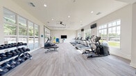 Located at 101 Cool Springs Dr in Elizabethtown, Kentucky, this well-equipped fitness center offers a generous single-floor layout designed to support a comprehensive workout experience. The space is divided into distinct exercise zones, seamlessly connected by a hallway that guides users through the facility.

The main workout area is bright and airy, featuring neutral-toned carpet flooring and white walls that create a clean, modern aesthetic. Recessed lighting and ceiling fans are distributed throughout, ensuring consistent illumination and airflow. Large multi-pane windows line the walls, flooding the space with abundant natural light and providing views of the surrounding greenery.

A notable architectural feature is the full-width glass garage door, which opens directly to an outdoor area, allowing for excellent ventilation and an open, connected feel. Multiple wall-mounted flat-screen televisions are positioned throughout, offering entertainment during workouts.

The cardio zone is well-appointed with a row of treadmills, elliptical trainers, a stationary bike, and a stair climber. A separate strength and functional training area houses a cable machine, weight bench, dumbbell rack, and resistance equipment. Medicine balls and additional accessories round out the fitness offerings. The overall ambiance is bright, spacious, and welcoming, making this fitness center a functional and inviting facility for residents of the Cool Springs community.