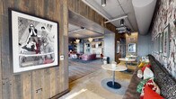 Located at 641 Division St in Nashville's vibrant Gulch neighborhood, this single-floor space is a masterclass in industrial-chic design. Exposed concrete ceilings with visible ductwork and piping contrast beautifully with warm reclaimed wood wall paneling and exposed brick, creating a layered, textural aesthetic throughout.

The open floor plan encompasses several distinct zones. A lounge area anchors the space with bold, patterned sofas, elegant crystal chandeliers, and an extensive curated gallery of black-and-white framed photography. An adjacent seating nook features a collage-style accent wall, built-in banquette seating, and polished concrete flooring. A game and entertainment area includes a regulation pool table and a dartboard, all bathed in abundant natural light from floor-to-ceiling windows.

A standout feature is the glass-enclosed piano alcove, where a grand piano sits beneath soaring windows offering panoramic views of the Nashville skyline — a dramatic and inspiring focal point. A private dining or conference area provides a round table with upholstered chairs, dual mounted displays, and additional curated artwork along exposed brick walls.

Throughout, wide-plank hardwood flooring, bold accent lighting, and thoughtfully placed sculptural décor pieces reinforce a cohesive, music-inspired identity that reflects Nashville's creative spirit.