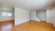 Located at 33 Kenneth St in West Haven, Connecticut, this multi-floor residential property spans three levels and offers a practical, well-organized layout across two bedrooms and one bathroom. The main living level features a generously sized living room with warm hardwood-style flooring, crisp white walls, and baseboard heating. A staircase with a metal railing connects the floors, providing a clean, functional transition between levels. The kitchen is equipped with warm wood-toned cabinetry, ample upper and lower storage, a white appliance suite including a range, dishwasher, and refrigerator, and a single-basin sink beneath a window that brings in natural light. The full bathroom features a tiled tub-shower surround in a classic white finish. Both bedrooms are carpeted in gray and feature white walls, windows with blinds offering natural light and outdoor views, and baseboard heating. The primary bedroom is notably spacious and includes a closet. The lower level consists of an unfinished basement with concrete floors, support columns, exposed utility systems, and small egress windows, offering significant storage or utility potential. Throughout the home, a neutral color palette and consistent finishes create a clean, move-in-ready atmosphere.