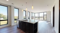 Located at 791 Morris Ave in Ashwaubenon, Wisconsin, this single-floor unit showcases a contemporary design defined by clean lines, modern finishes, and an abundance of natural light. Large, black-framed floor-to-ceiling windows are a defining architectural feature throughout, offering expansive outdoor views and flooding the interior with daylight.

The open-concept kitchen serves as the centerpiece of the living space, anchored by a substantial island with a light quartz countertop, an undermount sink, and a professional-style faucet. Dark espresso cabinetry extends to the ceiling along the back wall, complemented by stainless steel appliances—including a refrigerator, range, and built-in microwave—and a classic tile backsplash. Pendant lighting adds warmth above the island. The kitchen flows seamlessly into the living area, which features light wood-look flooring and corner window arrangements that maximize views on multiple sides.

The bedroom is carpeted for comfort and includes built-in shelving alongside a large window. Two bathrooms complete the unit: one with a walk-in shower and dark vanity cabinetry, and another with a full soaking tub/shower combo, both finished with light tile flooring and quartz countertops. The overall ambiance is polished and modern throughout.