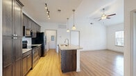 This two-story home in Lenexa, Kansas offers a thoughtfully designed layout spread across two floors. The main level features an open-concept kitchen and living area with warm hardwood-style flooring throughout. The kitchen is a standout, boasting dark espresso cabinetry reaching to the ceiling, granite countertops, a large center island with a built-in sink, stainless steel appliances, a tile backsplash, and pendant lighting complemented by a track light fixture. A dedicated laundry room with full-size washer and dryer hookups and a convenient garage with an automatic opener round out the lower level. The upper floor hosts all three bedrooms, including a generously sized primary suite featuring vaulted ceilings, a ceiling fan, a large window with natural light, and a walk-in closet with built-in wood shelving. The two bathrooms are finished with dark wood vanities, white quartz countertops, and light wood-style flooring. One bathroom includes a tub-shower combination with tiled surround, while the second offers a bright window for added ventilation. Additional bedrooms feature light hardwood-style flooring and vaulted ceilings, completing this clean, modern home.