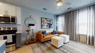 This thoughtfully designed single-floor residence blends modern aesthetics with practical functionality across a well-organized layout. The living area serves as the heart of the home, featuring soft blue-gray walls, warm wood-tone flooring, and a ceiling fan overhead. A rich cognac leather sofa anchors the space, complemented by a bold large-scale abstract artwork, a geometric patterned area rug, and floor-length striped drapes that frame windows allowing ample natural light.

The kitchen is a standout, showcasing two-tone cabinetry with crisp white uppers and charcoal gray lowers, a classic subway tile backsplash, and a full suite of stainless steel appliances. A central island with a white quartz countertop and seating provides an ideal space for casual dining, while pendant lights with glass shades add a refined touch overhead.

The bedrooms are bright and serene, each benefiting from large windows with blinds, ceiling fans, and wood flooring. Thoughtful storage is evident throughout, with utility areas including a dedicated laundry closet and additional storage spaces that enhance everyday convenience.

Throughout the residence, consistent light gray walls, clean trim work, and warm flooring create a cohesive, modern ambiance that is both inviting and versatile.