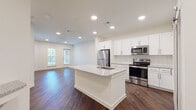 This single-floor residence offers a thoughtfully designed open-concept layout that seamlessly connects the kitchen and living areas. The kitchen is a standout feature, showcasing white shaker-style cabinetry, a classic subway tile backsplash, and a full suite of stainless steel appliances including a refrigerator, electric range, and built-in microwave. A central island with a granite countertop and undermount sink provides both additional workspace and a natural gathering point, while a stainless steel dishwasher adds convenience. Rich, dark hardwood-style flooring runs throughout the main living areas, complementing the crisp white walls and recessed lighting that keeps the space bright and inviting. A stylish sliding barn door adds a modern farmhouse touch near the entryway. The open living area is generously proportioned, bathed in natural light from large windows, and offers a clean, versatile canvas. The bedroom features plush carpeting, neutral walls, and a window with blinds that allows for natural light. The bathroom is well-finished with a granite-topped vanity, a large framed mirror, white subway tile shower-tub combo, and hardwood-style flooring, tying the cohesive design language together throughout the residence.