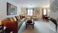 Located at 801 Cooper St in Deptford, NJ, this single-floor residence offers a well-organized layout that balances comfort and functionality throughout. The living room is generously sized, featuring soft wall-to-wall carpeting, neutral gray walls, and multiple windows dressed with elegant draping curtains that allow natural light to fill the space. The room comfortably accommodates a full seating arrangement centered around a rich wood coffee table, creating a welcoming atmosphere.

Adjacent to the living room, the dining area features its own window with draping curtains, a pendant light fixture overhead, and space for a full dining set — ideal for everyday meals or entertaining. The kitchen stands out with crisp white cabinetry, granite-style countertops, wood-look tile flooring, and a complete suite of stainless steel appliances, including a refrigerator, range, and over-the-range microwave.

The bedroom is a comfortable retreat with plush carpeting, natural window light, and ample space for a full bedroom set including a dresser with mirror. The bathroom is clean and modern, featuring a white vanity with updated hardware, wood-look tile flooring, and a tub/shower combination. Throughout the residence, a cohesive neutral palette and consistent finishes create a calm, livable environment.