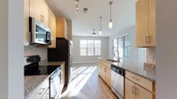 This single-floor, 3-bedroom residence offers a well-designed layout that balances functionality and modern style. The kitchen is a standout feature, equipped with stainless steel appliances including a refrigerator, electric range, built-in microwave, and dishwasher. Light wood cabinetry pairs elegantly with dark granite countertops, while pendant lighting and a track light fixture add both task and ambient illumination. The kitchen flows seamlessly into the living area, which is bathed in natural light from multiple windows and features a ceiling fan overhead — creating a bright, airy atmosphere ideal for everyday living and entertaining. Hardwood-style flooring extends consistently throughout the main living spaces, contributing to a cohesive and clean aesthetic. The hallway connects the bedrooms with crisp white panel doors, neutral warm-toned walls, and flush-mount ceiling lighting. HVAC venting is integrated into the ceiling, and ample closet access is available along the corridor. The overall design emphasizes clean lines, neutral tones, and practical finishes, making this a versatile and move-in-ready space suited for a variety of lifestyles.