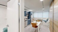 Located in the heart of downtown Oklahoma City at 520 W Main St, this efficiently designed studio presents a thoughtfully arranged open-plan layout that integrates the kitchen, dining, and living areas into a single cohesive space. The kitchen is a standout feature, outfitted with sleek blue cabinetry accented by matte black hardware, stainless steel appliances including a full-size refrigerator, built-in microwave, dishwasher, and a smooth countertop with a modern black-finish sink. Track lighting runs along the white ceiling, providing flexible, well-distributed illumination throughout. The living and sleeping area is bright and airy, benefiting from large roller-shade windows that allow soft, diffused natural light to fill the room. A wood-paneled wardrobe offers practical storage. The clean, light-toned flooring and neutral white walls create a fresh, modern ambiance. A separate full bathroom features a bathtub with shower, clean white finishes, and tile flooring. Every inch of this studio is optimized for comfortable urban living, making it an ideal space in the vibrant core of Oklahoma City.