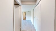 This well-appointed 2-bedroom, 1-bathroom apartment offers 960 square feet of single-floor living space with a clean, modern aesthetic throughout. Light wood flooring extends across the unit, creating a warm and cohesive feel from room to room.

The kitchen is a standout feature, showcasing walnut-toned cabinetry with matte black hardware, white quartz countertops, and a white tile backsplash. Stainless steel appliances include a French door refrigerator, gas range, over-the-range microwave, and dishwasher, complemented by a sleek black faucet at the undermount sink.

Both bedrooms are generously sized — the primary measuring 210 square feet — each featuring neutral walls, light wood floors, ceiling fans, and windows with blinds that frame greenery views. The full bathroom is finished with white tile surround in the tub/shower combo and matte black fixtures, maintaining the unit's consistent modern style.

Additional highlights include two living areas, a dedicated laundry room with a full-size washer, a hallway with closet storage, and a private balcony enclosed by a black metal railing that overlooks a lush tree canopy — providing a serene, nature-filled backdrop to everyday living.