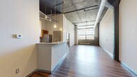 This striking 3-bedroom, 2-bathroom unit at 911 N 16th St in Omaha, Nebraska, showcases a bold industrial-chic aesthetic rooted in its converted warehouse heritage. Soaring exposed concrete ceilings with visible ductwork and structural columns define the character of the space throughout, complemented by rich hardwood-style flooring that runs seamlessly across every room.

The open-concept living area is expansive and light-filled, anchored by large factory-style windows that frame sweeping views of the surrounding cityscape. Exposed brick accents near the windows add warmth and texture to the raw industrial palette. Pendant Edison bulb lighting and track lighting enhance the loft-inspired ambiance.

The kitchen features warm honey-toned wood cabinetry, stainless steel appliances including a refrigerator, microwave, and range, and a generous peninsula with a built-in sink and counter seating — ideal for both cooking and entertaining.

The generously sized primary bedroom offers its own set of large factory windows with brick detailing, flooding the room with natural light. A standout feature is the dual closet system with wire-rack shelving, providing ample organized storage. The second bathroom includes a glass-enclosed shower, wood cabinetry, and stone-topped vanity, while the second bathroom offers a full tub-shower combo. Hardwood-style flooring carries throughout all bedrooms and bathrooms, maintaining a cohesive and polished industrial feel.