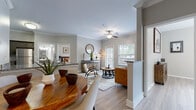 This thoughtfully designed single-floor residence offers a seamless blend of comfort and modern style throughout its open-concept layout. Light wood-look flooring flows continuously through the main living areas, complemented by neutral gray walls, crown molding, and ceiling fans that add to the refined character of the space.

The open living and dining area forms the heart of the home. The dining space features a dedicated nook framed by crown molding, providing a defined yet connected area for meals. The living room receives abundant natural light through large windows fitted with plantation shutters, creating a bright and welcoming atmosphere.

The kitchen is well-equipped with gray shaker-style cabinetry, granite countertops, a white subway tile backsplash, and a full suite of stainless steel appliances, including a gas range, microwave, refrigerator, and dishwasher. Light wood-look flooring and crown molding carry through here as well.

The bedroom is a calm retreat, featuring a ceiling fan, a large window with outdoor views, and direct access to a spacious walk-in closet with built-in shelving. The bathroom includes a granite-topped vanity with gray cabinetry, a tiled tub-shower combination, and light wood-look flooring. A dedicated utility area with tile flooring and a thermostat rounds out the functional amenities of this well-planned residence.
