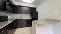 This two-floor residence offers a clean, functional layout designed for comfortable everyday living. The kitchen serves as a practical centerpiece, showcasing rich dark-espresso cabinetry with brushed hardware, granite countertops, and a full suite of black appliances including a refrigerator, dishwasher, and range. A peninsula with a matching granite surface provides additional prep space and casual seating, while light tile flooring ties the area together with a polished finish.

The bedrooms are carpeted in neutral tones, offering a warm and quiet atmosphere. Each room features clean white walls, ample natural light through blindeted windows, and generous floor space suitable for a variety of furnishing arrangements.

The space includes two full bathrooms, each featuring a tub and shower combination with white subway tile surround and brushed nickel fixtures. One bathroom also includes a dark-vanity with a framed mirror and tile flooring, maintaining a consistent design language throughout.

A half bathroom is also present, finished with a dark vanity cabinet, white countertop, framed mirror, and tile flooring for a neat and cohesive look. Throughout both floors, the neutral color palette and consistent finishes create a bright, understated ambiance that is both practical and inviting.