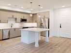 This thoughtfully designed 950-square-foot apartment offers 2 bedrooms and 2 bathrooms across a single floor, delivering a clean, modern aesthetic throughout. The open-concept kitchen and living area serves as the heart of the home, anchored by a large white-quartz island with built-in shelving. The kitchen features light wood-grain cabinetry, a white tile backsplash, stainless steel appliances including a refrigerator, range, microwave, and dishwasher, all illuminated by recessed lighting and globe pendant fixtures. Light wood-look flooring runs seamlessly throughout the entire unit. The primary bedroom, measuring 140 square feet, includes a ceiling fan, a large window for natural light, and direct access to a private balcony with exterior views. It is complemented by a spacious walk-in closet featuring multi-tiered wood hanging rods and shelving. The en-suite primary bathroom boasts a dual-sink blue vanity with white quartz countertops, a lighted mirror, and a tiled walk-in shower with a glass door. The second bedroom also features a ceiling fan and a bright window. The second bathroom mirrors the same refined design, with a blue vanity, lighted mirror, and a tiled tub-shower combination with matte black fixtures. A second closet provides additional storage throughout the unit.