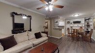This single-floor residence offers a well-organized layout with distinct living, dining, and kitchen areas that flow cohesively together. The living room serves as the central gathering space, featuring crown molding, a ceiling fan with light fixture, and durable wood-style plank flooring. A large ornate dark-framed mirror anchors one wall, complementing the built-in shelving unit that provides both storage and display space. The room accommodates comfortable seating centered around a wood coffee table, creating an inviting atmosphere.

The kitchen is accessible via a pass-through counter with a built-in wine rack above, offering a functional connection to the main living area. White cabinetry lines the galley-style kitchen, paired with granite-style countertops, a stainless steel sink, parquet tile flooring, and full appliances including a refrigerator and microwave.

Adjacent to the living room, a dedicated dining area features a round glass-top table set against a wall of built-in shelving, ideal for display and storage. A framed artwork adds a decorative focal point to the space.

The bathroom includes a tub-shower combination with a curtain enclosure, parquet flooring, and neutral wall tones consistent with the rest of the residence.