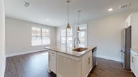Located at Annabelle on Main in Duluth, Georgia, this two-bedroom, two-bathroom residence is designed with a clean, modern aesthetic across a single-story layout. The interior is finished with dark wood-style plank flooring throughout the main living areas, complemented by neutral-toned walls and crisp white trim that create a bright, cohesive atmosphere.

The kitchen serves as a central focal point, anchored by a large island with granite countertops, an undermount sink, and open shelving below. Pendant lighting hangs above the island, while white shaker-style cabinetry, a subway tile backsplash, and stainless steel appliances—including a refrigerator, range, and microwave—complete the space. Multiple windows allow natural light to fill the adjacent dining area, which also features access to an exterior door with a gooseneck light fixture.

A well-lit hallway connects the bedrooms and bathrooms, lined with panel-style white doors and recessed lighting overhead. The bedrooms feature plush carpeting, ceiling fans, and windows with blinds. The bathrooms are finished with wood-look luxury vinyl flooring, a tub-shower combination, vanity with storage, and clean white fixtures throughout.