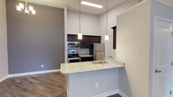 This single-floor residence offers a thoughtfully designed layout with modern finishes throughout. The kitchen serves as a focal point, featuring dark espresso cabinetry, granite countertops, and a full suite of stainless steel appliances including a range, microwave, and refrigerator. A peninsula with an undermount sink and pendant lighting above creates a natural division between the kitchen and the open living area, which transitions seamlessly from wood-look flooring to plush carpeting. The living space benefits from ceiling fans and a clean, neutral color palette that enhances the sense of openness. The bedrooms are carpeted and well-sized, each with ceiling fans and natural light provided by windows with blinds. Two bathrooms serve the residence: one features a tub-shower combo with dark tile surround and a granite-topped vanity, while the other includes a glass-enclosed walk-in shower with matching dark tile and a granite vanity. A standout feature is the expansive walk-in closet, equipped with abundant wire shelving and hanging rods for exceptional storage. Throughout the residence, consistent use of granite surfaces, dark cabinetry, and wood-look flooring creates a cohesive and contemporary aesthetic.