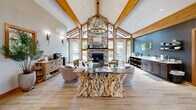 The Stevens Creek Apartments clubhouse at 11430 SE Stevens Rd in Happy Valley, Oregon, is a thoughtfully designed amenity space that combines rustic elegance with modern functionality. The grand entrance welcomes visitors through double glass doors beneath a soaring vaulted ceiling supported by exposed timber framing, setting the tone for the craftsmanship found throughout.

The centerpiece of the space is a stunning great room featuring dramatic vaulted ceilings with heavy wood beam accents, light hardwood-style flooring, and a floor-to-ceiling stacked stone fireplace that anchors the room with natural warmth. A striking driftwood-base glass coffee table serves as a focal point, surrounded by comfortable seating. Large windows and glass doors flood the room with natural light and offer views of the surrounding greenery.

Adjacent dining areas provide comfortable spaces for residents to gather, while a well-appointed conference room offers a large wooden table, leather chairs, a wall-mounted display, and its own climate control — ideal for meetings or private use.

The dedicated office space features a professional setup with carpeted flooring, a workstation, and refined cabinetry. The fitness center is generously equipped with a multi-station weight machine, treadmills, a cable machine, free weights, and kettlebells, all beneath vaulted ceilings with wood-trimmed windows that bring in natural light.