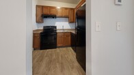 Located at 3031 Beech Grove Ct in Jeffersonville, Indiana, this single-floor, two-bedroom, one-bathroom unit offers a practical and straightforward layout across a compact but efficiently organized footprint. The living area is carpeted in neutral tones and features a textured ceiling, a ceiling-mounted light fixture, and a sliding glass door fitted with vertical blinds that provides natural light and outdoor views of a grassy exterior. A pass-through window connects the living area to the kitchen, adding a degree of openness between the two spaces.

The kitchen is equipped with wood-tone cabinetry, granite-look countertops, and a full suite of black appliances, including a range, refrigerator, and dishwasher. Durable wood-look vinyl flooring runs throughout the kitchen, offering a practical contrast to the carpeted areas elsewhere in the unit.

The spacious primary bedroom features soft carpet, white walls, a textured ceiling, and a closet with bifold doors, providing functional storage. The second bedroom is similarly finished with carpet and clean white walls. The bathroom includes a full-sized tub and shower combination with white tile surround and chrome fixtures. Throughout the unit, the clean, neutral palette and consistent finishes create a simple, functional living environment.