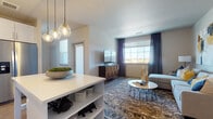 This well-appointed single-floor residence offers a thoughtfully designed open-concept layout that seamlessly connects the kitchen, dining, and living areas. The kitchen is a standout feature, showcasing crisp white shaker cabinetry, a light geometric tile backsplash, stainless steel appliances including a range, microwave, dishwasher, and refrigerator, and a generous island with a clean white countertop illuminated by globe pendant lights. Light wood-style flooring runs throughout the kitchen and living spaces, adding warmth and continuity.

The living room is bright and welcoming, with large windows dressed in navy curtains that allow natural light to flow in while offering views of the surrounding landscape. The space is accented by bold abstract artwork in navy and gold tones, adding a vibrant design focal point.

The primary bedroom features neutral carpet, a large window with sheer curtains, and a calm, restful ambiance. The secondary bedroom makes a striking impression with a deep navy accent wall, carpeted flooring, and a walk-in closet.

The full bathroom is finished with wood-look flooring, white cabinetry, a quartz-style countertop, and a tub-shower combination with elegant marble-style tile surround, completing this modern and cohesive living space.