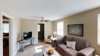 This single-floor residence offers a practical and comfortable layout designed for easy living. The living room serves as the heart of the home, featuring warm neutral-toned walls, plush carpeting, and a ceiling fan that adds both style and functionality. Natural light filters in through blinds-covered windows, creating a bright and welcoming atmosphere. Built-in shelving and closet storage add to the room's versatility.

The kitchen is efficiently designed, featuring light maple cabinetry, dark granite-style countertops, a stainless steel sink, and black appliances including a gas range and over-the-range microwave — providing everything needed for everyday cooking.

Two well-sized bedrooms continue the home's warm, neutral color palette, each equipped with ceiling fans, carpeted floors, and ample natural light from multiple windows. One bedroom includes a dedicated closet, while the other benefits from a cast iron radiator for supplemental heating. Both rooms offer a calm, restful ambiance.

The full bathroom is clean and functional, featuring a tiled tub-and-shower combination with a curved curtain rod, a window for natural ventilation, and classic white finishes throughout. The overall design of this residence is cohesive and practical, offering comfortable, move-in-ready living across every room.