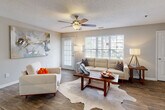 This single-floor residence offers a well-organized layout with distinct living, dining, kitchen, and sleeping areas connected by a cohesive design palette of neutral tones and wood-style flooring. The open living room is a welcoming focal point, featuring large windows with plantation shutters that invite abundant natural light and outdoor views, complemented by a ceiling fan and direct access to an exterior door. A cowhide-style area rug and contemporary artwork add character to the space.

The galley-style kitchen is efficiently designed with white cabinetry, granite countertops, a subway tile backsplash, stainless steel sink, and black appliances, including a refrigerator and electric range. A breakfast bar provides a natural transition into the open-plan layout. Adjacent to the kitchen, the dining area accommodates a round table beneath a pendant light fixture, with wainscoting detail along the walls.

The bedroom offers plush carpeting, a ceiling fan, a window with outdoor views, and access to a generously sized walk-in closet with wrap-around wire shelving. The bathroom features granite countertops, a large vanity mirror, white cabinetry, and a shower-tub combination. Textured ceilings are present throughout the residence.