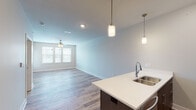 This single-floor residence showcases a contemporary open-concept design that seamlessly connects the kitchen and living area. The kitchen is a standout feature, equipped with dark espresso cabinetry, crisp white quartz countertops, a subway tile backsplash, and a full suite of stainless steel appliances, including a refrigerator, electric range, and built-in microwave. A central island with an undermount sink and pendant lighting overhead adds both functionality and visual appeal. Wood-look flooring runs throughout the main living areas, complementing the neutral gray wall tones and clean white trim.

The open living area is spacious and bright, benefiting from natural light through slatted windows and a ceiling fan for added comfort. The bedrooms are carpeted for warmth, each featuring ceiling fans and windows that allow natural light. The primary bedroom includes access to a walk-in closet and an en-suite bathroom, which features a soaking tub, tiled surround, a wide vanity with quartz countertops, dark cabinetry, and hardwood-style flooring. Additional rooms visible in the floorplan view suggest flexible living arrangements. Overall, the space presents a clean, modern aesthetic with consistent, quality finishes throughout.