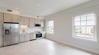Located at 181 North Main Street in Suffolk, Virginia, this thoughtfully designed 2-bedroom, 1-bathroom residence offers a clean, modern aesthetic throughout. The open-concept living and kitchen area is bathed in natural light, courtesy of multiple double-hung windows that frame views of the surrounding city. The kitchen is outfitted with stainless steel appliances — including a range, dishwasher, refrigerator, and microwave — complemented by gray shaker-style cabinetry, a herringbone tile backsplash, and recessed lighting overhead. Light-toned flooring flows seamlessly across the entire living space, reinforcing the bright and airy atmosphere. The spacious primary bedroom is a standout, featuring three large windows on two walls that flood the room with natural light and provide sweeping outdoor views, along with a ceiling fan for added comfort. The second bedroom offers similar light-filled character. The bathroom is finished with white cabinetry, a single-sink vanity with brushed gold hardware, a tub-shower combination, and tile flooring. Entry to the unit is secured with a keypad-enabled smart lock, adding a modern convenience. The overall design palette — soft whites, warm neutrals, and brushed gold accents — creates a cohesive and inviting living environment.