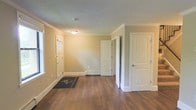 This two-floor space presents a well-maintained interior defined by consistent, neutral finishes and a practical layout. The main level entry area showcases warm hardwood-style flooring that extends throughout, complemented by crisp white baseboards and door trim that contrast neatly against the beige-toned walls. Crown moulding adds a refined architectural detail to the ceiling line, elevating the overall finish of the space.

The entry point features a panelled front door with sidelights, allowing natural light to filter into the main area. A welcome mat marks the threshold, grounding the entryway. Multiple white panelled interior doors lead to adjoining rooms, suggesting a functional and well-divided floor plan. A baseboard heater is visible along the rear wall, indicating an efficient heating setup suited for year-round comfort.

The space is illuminated by a ceiling-mounted light fixture, providing even ambient lighting. The overall aesthetic is clean, neutral, and move-in ready, with a cohesive design language maintained across visible surfaces. The two-floor configuration further expands the available living or working areas beyond what is visible in the main level.