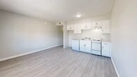 Located at 1311 Louisiana Blvd NE in Albuquerque, New Mexico, this efficiently designed single-floor unit makes smart use of its compact footprint. The layout centers around an open-plan living, dining, and kitchen area, where light gray luxury vinyl plank flooring runs seamlessly throughout, lending a clean and cohesive look to the space. The kitchen is positioned along one wall and features white cabinetry with ample upper storage, a white electric range, dishwasher, and a single-basin sink — all finished in a bright, neutral palette. A textured popcorn ceiling adds classic character overhead, while a wall-mounted light fixture and flush ceiling light provide functional illumination. The living and dining area benefits from a window that allows natural light to fill the room, offering views to the exterior. A hallway connects the main living space to the bathroom and three closets, providing notable storage capacity for a unit of this size. The bathroom is appointed with tile wainscoting in warm earth tones, a pedestal sink, and a full tub/shower combination with chrome fixtures. Throughout the unit, crisp white trim and neutral gray walls create a bright, move-in-ready atmosphere well-suited for efficient, comfortable living.