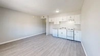 Located at 1311 Louisiana Blvd NE in Albuquerque, New Mexico, this efficiently designed single-floor unit makes smart use of its compact footprint. The layout centers around an open-plan living, dining, and kitchen area, where light gray luxury vinyl plank flooring runs seamlessly throughout, lending a clean and cohesive look to the space. The kitchen is positioned along one wall and features white cabinetry with ample upper storage, a white electric range, dishwasher, and a single-basin sink — all finished in a bright, neutral palette. A textured popcorn ceiling adds classic character overhead, while a wall-mounted light fixture and flush ceiling light provide functional illumination. The living and dining area benefits from a window that allows natural light to fill the room, offering views to the exterior. A hallway connects the main living space to the bathroom and three closets, providing notable storage capacity for a unit of this size. The bathroom is appointed with tile wainscoting in warm earth tones, a pedestal sink, and a full tub/shower combination with chrome fixtures. Throughout the unit, crisp white trim and neutral gray walls create a bright, move-in-ready atmosphere well-suited for efficient, comfortable living.