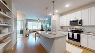 Located at 3239 Memorial Blvd in Murfreesboro, TN, this 1-bedroom unit offers a thoughtfully designed open-concept floor plan spread across a single level. The kitchen is a standout feature, showcasing crisp white shaker cabinetry, subway tile backsplash, granite countertops, and a full suite of stainless steel appliances. A large central island with pendant lighting above provides additional prep space and casual seating, flowing seamlessly into the living and dining areas. The living room is bright and welcoming, with large windows that invite natural light and a ceiling fan overhead. A signature teal accent wall adds a bold yet cohesive design element carried throughout the space. The bedroom is a comfortable retreat featuring plush carpeting, generous windows, and a stylish accent wall with a herringbone-patterned wallcovering. It connects directly to a well-sized bathroom with a dual-sink vanity, granite countertops, white cabinetry, and wood-look flooring. Throughout the unit, warm hardwood-style flooring ties the main living areas together, while recessed lighting and modern fixtures contribute to the overall polished aesthetic. The unit combines contemporary design with functional living.