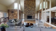 Located at 6592 Steinway Dr in Reynoldsburg, Ohio, this single-story space makes an immediate impression with its grand, open great room. The centerpiece of the room is a towering floor-to-ceiling stacked stone fireplace, framed by matching stone accent walls that extend the full height of the space, lending a rustic yet refined character throughout. Soaring vaulted ceilings amplify the sense of openness, while large windows positioned high along the walls flood the interior with generous natural light, creating a bright and welcoming atmosphere. The great room features warm hardwood flooring that contrasts beautifully with the cool, textured stonework, and the open layout comfortably accommodates a generous seating arrangement centered around the fireplace. The combination of natural materials — stone, wood, and neutral-toned furnishings — establishes a cohesive, inviting aesthetic. The architectural design emphasizes verticality and volume, making the space feel expansive and airy. Overall, this property offers a distinctive blend of natural craftsmanship and open-plan living, centered around a dramatic architectural focal point that defines the character of the entire space.