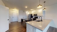 Located at 122 Parsons Ave in Columbus, Ohio, this contemporary two-floor residence offers a well-appointed layout with modern finishes throughout. The main level features an open-concept kitchen and living area anchored by rich hardwood flooring. The kitchen is outfitted with white shaker cabinetry, a classic subway tile backsplash, stainless steel appliances including a refrigerator, range, and over-the-range microwave, and a large center island with a quartz countertop and matte black fixtures. Stylish pendant lighting adds a warm, modern touch overhead. The main floor also includes a staircase leading to the upper level, closet storage, and utility access. The upper floor hosts generously sized bedrooms with plush carpeting and large windows that invite abundant natural light. One bedroom offers a striking triple-window view of the Columbus skyline, while another features a similar multi-window layout with neighborhood views. The bathroom is finished with white subway tile in the walk-in shower with a glass enclosure, taupe floor tile, a white vanity with quartz countertop, and matte black fixtures and hardware, providing a clean and cohesive aesthetic throughout the space.