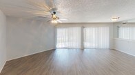 This single-floor unit offers a clean, functional layout designed for comfortable everyday living. The living area is a bright, open space anchored by wood-style laminate flooring and a ceiling fan with integrated lighting. Large sliding glass doors dressed with vertical blinds allow generous natural light to fill the room and provide direct access to an outdoor area. An additional room features a similar sliding glass door, extending the connection to the outdoors.

The kitchen is efficiently designed with crisp white cabinetry, dark speckled countertops, a black electric range with overhead ventilation, and a stainless steel sink. A hallway connects the kitchen to the rest of the unit, providing a natural flow between spaces.

The bedrooms feature the same wood-style flooring found throughout, neutral gray walls, and textured ceilings. One bedroom includes a built-in closet with bifold doors and a window with blinds that brings in natural light. Additional rooms offer open wall space well-suited for flexible use.

The bathroom is finished with neutral tones and includes a walk-in shower stall with white tile surround, a grab bar, and a toilet. Throughout the unit, consistent finishes — including white trim, textured ceilings, and coordinated flooring — create a cohesive and move-in-ready atmosphere.