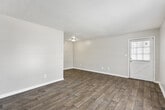 This single-story, 1-bedroom, 1-bathroom unit offers a practical and comfortable layout designed to maximize every square foot. The open living area greets you upon entry, featuring warm wood-look laminate flooring, neutral-toned walls, and a textured ceiling that adds subtle character. Natural light filters in through a window fitted with blinds, keeping the space bright and airy. The living area flows seamlessly into the kitchen, which is equipped with white cabinetry featuring gold-tone hardware, light-colored countertops, a stainless sink, and black appliances including a range and refrigerator — offering ample functionality for everyday cooking. The generously sized bedroom is carpeted for added comfort and includes two closets for convenient storage. A sliding glass door with vertical blinds opens to an outdoor view, filling the room with natural light. The bathroom features wood-look flooring, a single-sink vanity with a light countertop, and decorative oval mirrors above, complemented by a well-lit vanity fixture. A dedicated closet provides additional storage within the unit. The consistent neutral palette and cohesive finishes throughout create a clean, move-in-ready atmosphere suited for a variety of living styles.