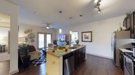 This single-floor residence offers a thoughtfully designed open-concept layout that seamlessly connects the kitchen, dining, and living areas. The kitchen is a standout feature, equipped with dark espresso cabinetry, granite countertops, a tile backsplash, stainless steel appliances including a side-by-side refrigerator, range, microwave, and dishwasher, and a central island with a sink and pendant lighting above. Rich hardwood-style flooring runs throughout the main living areas, adding warmth and continuity to the space.

The living room is bright and inviting, with a ceiling fan, natural light from large windows with blinds, and access to a patio via French doors. Multiple bedrooms are carpeted for comfort, each featuring ceiling fans and windows that allow for natural light. The bedrooms are served by well-organized closets, including a spacious walk-in closet with wire shelving systems offering ample storage.

The bathroom is finished with tile flooring, dark wood vanity cabinetry, granite countertops, large mirrors, and tile-surround walls. The floor plan also includes a dedicated flex room, visible in the dollhouse view, suitable for use as a home office or workout space. Throughout the unit, a consistent palette of neutral tones, modern fixtures, and quality finishes creates a cohesive and comfortable living environment.