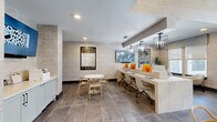 Located at 1876 Star Anise Cir in Apopka, FL, this single-floor community amenity space delivers a polished, contemporary environment designed for productivity, collaboration, and relaxation. The layout encompasses a business center, a private conference room, a welcoming lounge area, and a well-appointed kitchenette, all unified by large-format stone-look tile flooring and textured geometric wallcoverings throughout.

The business center features a long, sleek workstation lined with desktop computers, pendant lighting overhead, and a mounted flat-screen display, creating an efficient and professional workspace. An adjacent seating area with modern accent chairs offers a comfortable spot for casual meetings or quiet work.

A glass-walled conference room provides a semi-private setting equipped with a conference table and rolling chairs, maintaining visual connectivity to the main space. A separate meeting nook with blue upholstered chairs and natural light from large windows adds additional flexibility.

The kitchenette is outfitted with light blue shaker-style cabinetry, a geometric tile backsplash, white quartz countertops, a black matte sink, a beverage refrigerator, and open shelving styled with decorative accents.

The lounge area benefits from soaring windows that flood the space with natural light and offer views of lush outdoor greenery, while elegant wingback chairs and curated artwork contribute to a refined, inviting atmosphere throughout.