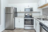 Located at 34835 Utica Rd in Fraser, Michigan, this single-floor unit offers a clean, modern interior with a neutral color palette throughout. The kitchen is well-appointed with stainless steel appliances, including a refrigerator, electric range, and over-the-range microwave, all complemented by white shaker-style cabinetry and light granite-style countertops. Wood-look plank flooring runs through the kitchen and living areas, adding warmth and continuity. The dining area sits adjacent to the kitchen and features a chandelier overhead, creating a defined yet open space. The living room benefits from natural light through a sliding glass door that opens to an outdoor view, with vaulted ceiling lines adding to the sense of openness. Bedrooms are carpeted for comfort and include generous closet space, highlighted by a spacious walk-in closet with wire shelving. The bathroom features a dual-sink vanity with white cabinetry, granite-style countertops, wood-look flooring, and a soaking tub. Overall, the unit presents a bright, well-maintained interior with practical finishes throughout.