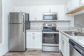 Located at 34835 Utica Rd in Fraser, Michigan, this single-floor unit offers a clean, modern interior with a neutral color palette throughout. The kitchen is well-appointed with stainless steel appliances, including a refrigerator, electric range, and over-the-range microwave, all complemented by white shaker-style cabinetry and light granite-style countertops. Wood-look plank flooring runs through the kitchen and living areas, adding warmth and continuity. The dining area sits adjacent to the kitchen and features a chandelier overhead, creating a defined yet open space. The living room benefits from natural light through a sliding glass door that opens to an outdoor view, with vaulted ceiling lines adding to the sense of openness. Bedrooms are carpeted for comfort and include generous closet space, highlighted by a spacious walk-in closet with wire shelving. The bathroom features a dual-sink vanity with white cabinetry, granite-style countertops, wood-look flooring, and a soaking tub. Overall, the unit presents a bright, well-maintained interior with practical finishes throughout.