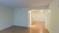 This two-floor space presents a straightforward and functional layout characterized by clean lines and a neutral color palette. The interior features light hardwood flooring that extends throughout the main living areas, contributing warmth and continuity to the space. Walls are finished in a soft, off-white tone that reflects light and enhances the overall brightness of the interior.

The main level showcases an open flow between rooms, with a wide doorway connecting two distinct areas. The adjoining room is fitted with vertical blinds spanning a large window or sliding door, allowing for adjustable natural light and suggesting potential access to an outdoor area. A ceiling-mounted light fixture provides additional illumination in this space.

A overhead HVAC vent is visible, indicating a centralized climate control system. The layout includes interior doors that help define separate functional zones while maintaining an open and airy feel. The two-floor configuration of the space provides added versatility, offering separation between living and private areas. Overall, the space conveys a clean, move-in ready environment with practical finishes suited for everyday living.