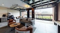 Located at 220 N Patterson Blvd in Dayton, Ohio, this single-floor premium stadium suite delivers an exceptional game-day experience with a seamless blend of comfort and access. The centerpiece of the space is a sophisticated lounge area featuring large-format tile flooring, exposed brick accent walls, and a dramatic glass-paneled garage door that opens fully to an outdoor balcony. From the balcony, guests enjoy unobstructed views of the baseball field below, complete with stadium seating directly accessible from the suite. The interior lounge is furnished with plush sofas, leather club chairs, and wooden accent tables, creating an inviting atmosphere ideal for entertaining. Multiple wall-mounted flat-screen televisions ensure the action is never missed from any vantage point. A dedicated kitchenette supports the suite's hosting capabilities, featuring wood-toned cabinetry with gold hardware, a stainless steel sink, a full-size stainless steel refrigerator, a stovetop, and ample counter space with a clean white surface. The overall design balances industrial character — through exposed brick and dark metal framing — with polished, modern finishes, resulting in a sophisticated and functional private event space suited for corporate gatherings, group outings, or special occasions.