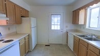 This three-floor space offers a straightforward and functional layout designed for comfortable everyday living. The kitchen is arranged in a galley-style configuration, with light wood cabinetry lining both sides and providing ample storage. White appliances, including a full-size refrigerator and dishwasher, complement the neutral countertops and light-toned tile flooring. A paneled exterior door with a windowed insert anchors the far end of the kitchen, allowing natural light to filter in and offering convenient direct outdoor access.

The living area presents a bright, open atmosphere enhanced by neutral carpet flooring and white walls that lend a clean, versatile backdrop. A large sliding glass door dominates one wall, flooding the room with abundant natural light and framing views of a lush green outdoor area. A secondary window on the adjacent wall further enhances the sense of openness and airiness throughout the space. The overall ambiance across the home is clean and understated, with a neutral palette throughout that offers a welcoming foundation adaptable to a variety of interior styles. The three-floor layout provides additional flexibility for various living arrangements.