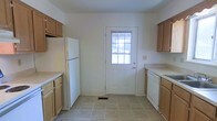This three-floor space offers a straightforward and functional layout designed for comfortable everyday living. The kitchen is arranged in a galley-style configuration, with light wood cabinetry lining both sides and providing ample storage. White appliances, including a full-size refrigerator and dishwasher, complement the neutral countertops and light-toned tile flooring. A paneled exterior door with a windowed insert anchors the far end of the kitchen, allowing natural light to filter in and offering convenient direct outdoor access.

The living area presents a bright, open atmosphere enhanced by neutral carpet flooring and white walls that lend a clean, versatile backdrop. A large sliding glass door dominates one wall, flooding the room with abundant natural light and framing views of a lush green outdoor area. A secondary window on the adjacent wall further enhances the sense of openness and airiness throughout the space. The overall ambiance across the home is clean and understated, with a neutral palette throughout that offers a welcoming foundation adaptable to a variety of interior styles. The three-floor layout provides additional flexibility for various living arrangements.