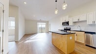 This single-floor residence offers a clean, contemporary design highlighted by an open-concept layout that seamlessly connects the kitchen and living area. The kitchen serves as a central focal point, featuring a large island with dark countertops and a warm natural wood base, white shaker-style cabinetry, a dark stone backsplash, and a full suite of stainless steel appliances including a range, microwave, and refrigerator. Decorative pendant lights hang above the island, adding a stylish finishing touch. The adjacent living area is bright and airy, benefiting from a large sliding glass door that opens to a private balcony with outdoor views, allowing generous natural light to pour across the light hardwood-style flooring.

The bedrooms are comfortably sized, with one featuring plush carpeting and another with hardwood-style flooring and a window offering neighborhood views. Storage is well-addressed throughout, with a spacious walk-in closet outfitted with wire shelving systems. The bathroom includes a light wood vanity with white countertops, a mirror, and a shower-tub combination. A dedicated laundry room houses a full-sized Whirlpool washer and dryer set with overhead wire shelving. Throughout the unit, neutral tones and recessed lighting create a bright, cohesive ambiance.
