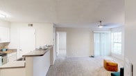This single-floor residence offers a clean, functional layout designed for comfortable everyday living. The open-concept living area flows seamlessly from the kitchen, which is equipped with white cabinetry, laminate wood-style flooring, a stainless steel electric range, a refrigerator, and ample counter space. A breakfast bar with a dark countertop provides a convenient transition between the kitchen and the living space, which features plush wall-to-wall carpeting, a ceiling fan, and a sliding glass door with vertical blinds that invites natural light. The bedroom is generously sized with soft carpeting, a window fitted with blinds, and direct access to a walk-in closet. An en-suite bathroom includes a wide vanity with a single sink, a large mirror illuminated by a strip light fixture, and a full tub-shower combination with white tile surround. A dedicated in-unit laundry area houses a top-loading washer alongside built-in shelving for storage. Throughout the space, neutral tones, textured ceilings, and consistent finishes create a bright, cohesive atmosphere that is easy to personalize.