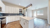 Located at 600 Calvert St in Charlotte, NC, this single-floor residence combines modern design with functional living. The open-concept kitchen is a standout feature, showcasing white shaker cabinetry with gold and silver hardware, a blue-gray subway tile backsplash, quartz countertops, a farmhouse sink, stainless steel appliances, and a central island with a contemporary rectangular pendant light. The kitchen flows seamlessly into the living area, which is finished with warm hardwood-style flooring and a ceiling fan, with a glass door inviting natural light from outside. The bedrooms are bright and airy, featuring large windows fitted with blinds that frame views of the Charlotte skyline and surrounding greenery, with sunlight reflecting off the light hardwood floors. The primary bathroom is elegantly appointed with marble-look tile flooring, a glass-enclosed walk-in shower with marble-style tile surround, a granite-topped vanity with blue cabinetry, and direct access to a well-organized walk-in closet. A second full bathroom offers marble-look tile floors, a granite vanity with gray cabinetry, a backlit mirror, and a tub-shower combination. A dedicated laundry room houses a full-size washer and dryer with overhead wire shelving for added storage.