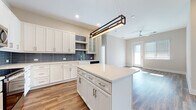 Located at 600 Calvert St in Charlotte, NC, this single-floor residence combines modern design with functional living. The open-concept kitchen is a standout feature, showcasing white shaker cabinetry with gold and silver hardware, a blue-gray subway tile backsplash, quartz countertops, a farmhouse sink, stainless steel appliances, and a central island with a contemporary rectangular pendant light. The kitchen flows seamlessly into the living area, which is finished with warm hardwood-style flooring and a ceiling fan, with a glass door inviting natural light from outside. The bedrooms are bright and airy, featuring large windows fitted with blinds that frame views of the Charlotte skyline and surrounding greenery, with sunlight reflecting off the light hardwood floors. The primary bathroom is elegantly appointed with marble-look tile flooring, a glass-enclosed walk-in shower with marble-style tile surround, a granite-topped vanity with blue cabinetry, and direct access to a well-organized walk-in closet. A second full bathroom offers marble-look tile floors, a granite vanity with gray cabinetry, a backlit mirror, and a tub-shower combination. A dedicated laundry room houses a full-size washer and dryer with overhead wire shelving for added storage.