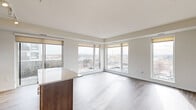 This thoughtfully designed 2-bedroom, 3-bathroom single-floor residence offers a bright, modern living experience highlighted by an abundance of natural light and panoramic urban views. The open-concept living and dining area flows seamlessly from the kitchen, which features warm wood cabinetry, granite countertops, a white subway tile backsplash, stainless steel appliances, a peninsula island, and track lighting overhead. Large floor-to-ceiling windows wrap the living space, filling the room with daylight and framing wide views of the surrounding cityscape and distant mountains. Durable wood-look flooring runs throughout the main living areas, while plush carpet adds comfort to the bedrooms. The spacious primary bedroom includes generous walk-in closet space with wire shelving, and an en-suite bathroom outfitted with a double-sink vanity, granite countertops, dark wood cabinetry, a large mirror, and tile flooring. The second bedroom also benefits from a large window with city views. Additional bathrooms include a clean, all-white shower unit. A connecting hallway with crisp white shaker-style doors ties the layout together cohesively, contributing to the unit's clean and contemporary aesthetic throughout.