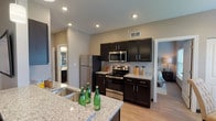 This single-floor residence in Shiloh, Illinois, offers a thoughtfully designed open-concept layout that seamlessly connects the living, dining, and kitchen areas. Light wood-tone flooring runs throughout, complementing the neutral gray and beige color palette that gives the space a clean, contemporary feel.

The living area is generously sized, featuring a ceiling fan, multiple windows with slatted blinds that allow ample natural light, and a dedicated wall-mounted television nook. A dining area positioned near a large window provides an inviting spot with natural views. The kitchen is well-equipped with dark cabinetry, granite-style countertops, stainless steel appliances including a refrigerator, range, and microwave, and a breakfast bar with pendant lighting overhead.

The bedrooms are comfortably scaled, each featuring ceiling fans, windows for natural light, and access to walk-in closets. The bathroom includes dark cabinetry vanity with a large mirror and wood-look flooring consistent with the rest of the unit.

A dedicated hallway leads to a practical in-unit laundry closet with a stacked washer and dryer. The overall layout is efficient and well-organized, offering comfortable, modern living in a cohesive, neutral aesthetic.